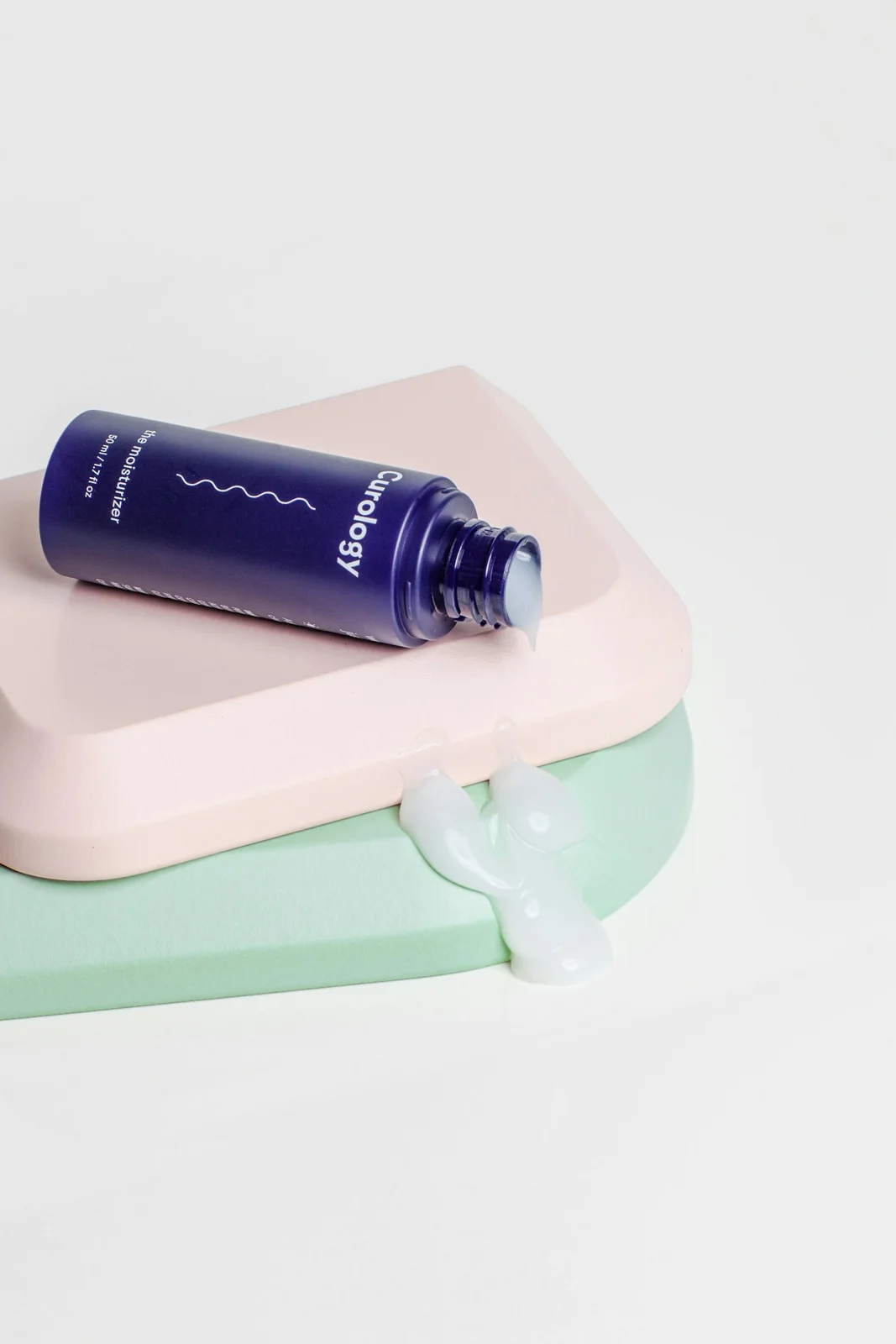 A purple skincare bottle on a pastel pink surface