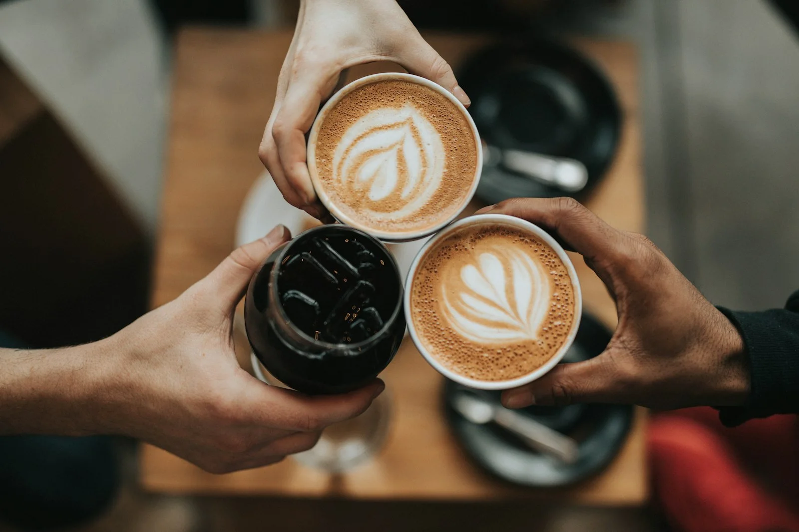 Hands holding three cups of coffee with decorative foam
